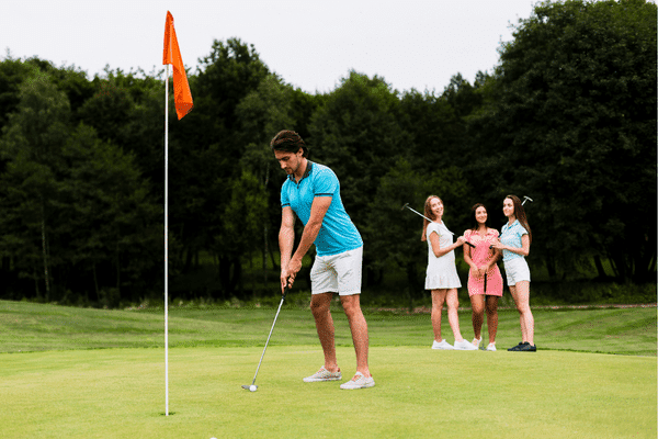 Man putting golf ball watched by three women